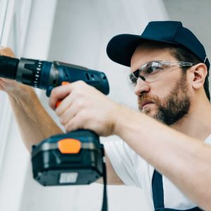 adult-repairman-in-goggles-fixing-window-handle-by-electric-drill-e1663969255653.jpg